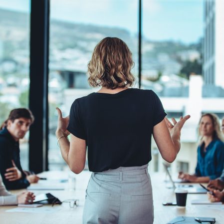 A lady speaking to a team of people seated at a table in a boardroom.