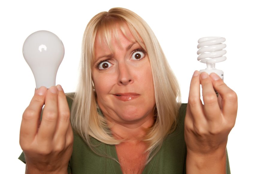 Funny Faced Woman Holds Energy Saving and Regular Light Bulbs Isolated on a White Background.