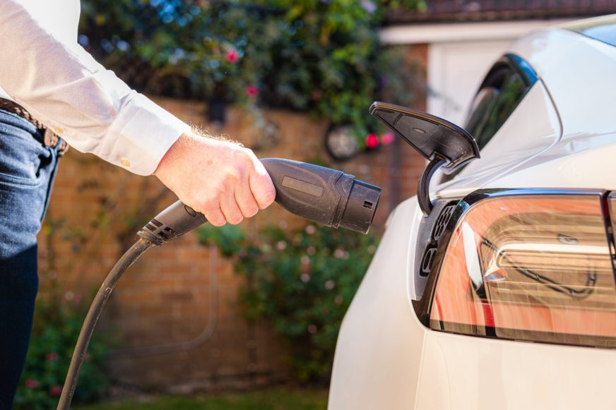 Color image depicting a man charging his electric vehicle at home.