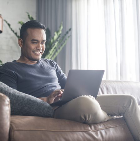 Young Asian man using the laptop in the living room.